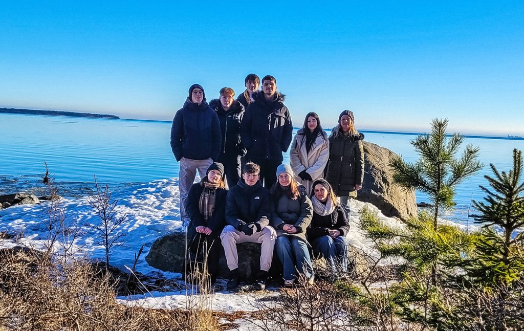 Gruppbild med skolklass som står i skog framför sjö.
