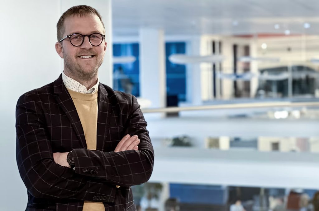 Bild på lärare som står med armarna i kors, bär kostym.