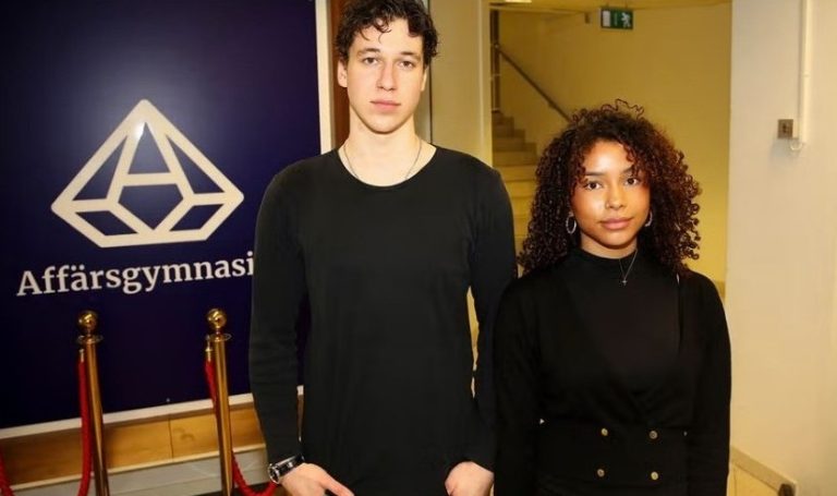 Två unga elever i mörka kläder står framför en skylt med texten Affärsgymnasiet