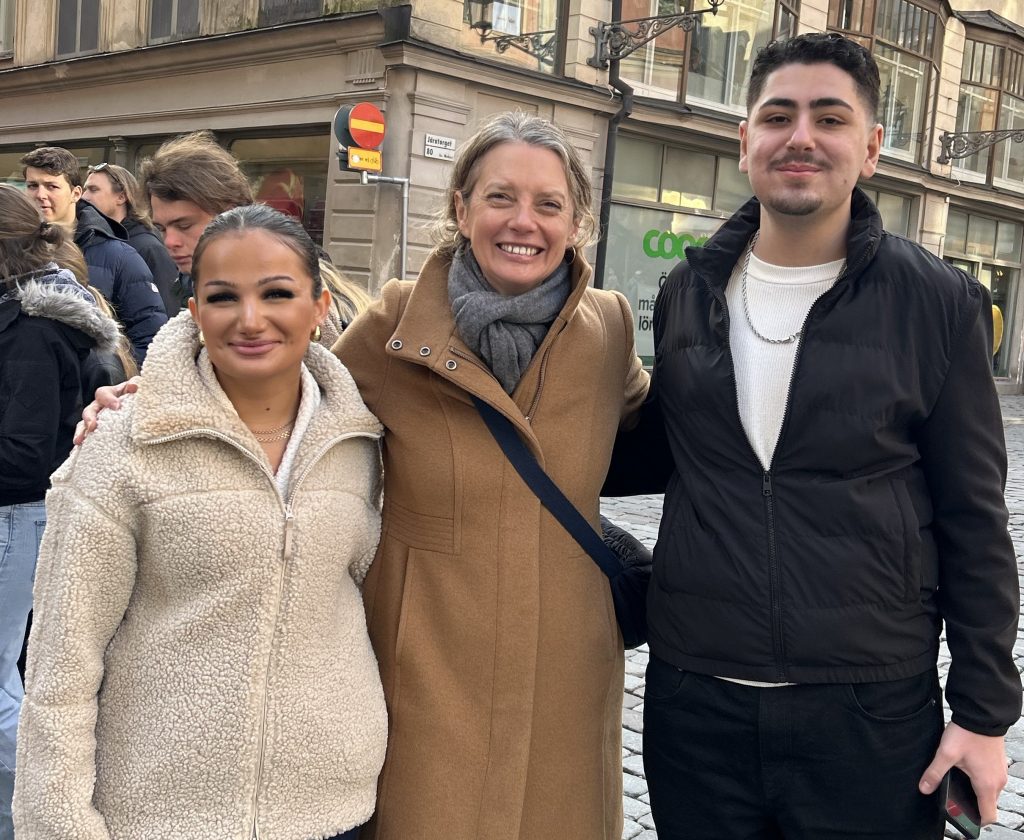 En lärare och två elever ler mot kameran på Järntorget i Gamla stan